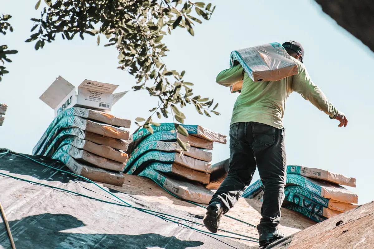 Roofer carrying a bundle of shingles across a roof deck during a reroof